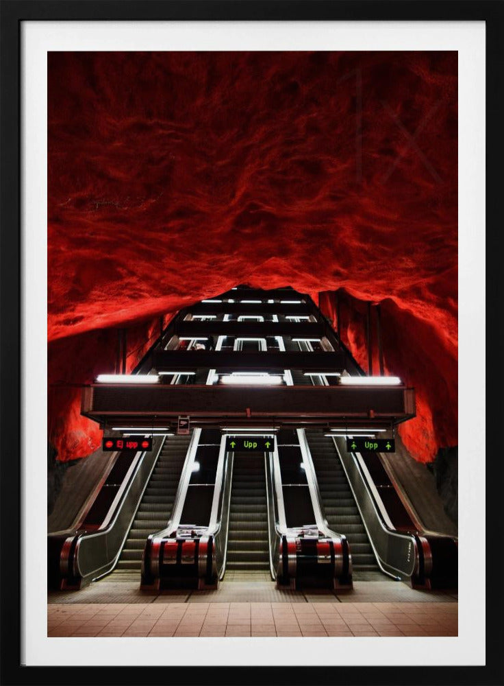 A dramatic low-angle shot looking up a series of escalators in a subway station with a cavernous, rough-textured ceiling glowing an intense, fiery red. Decor
