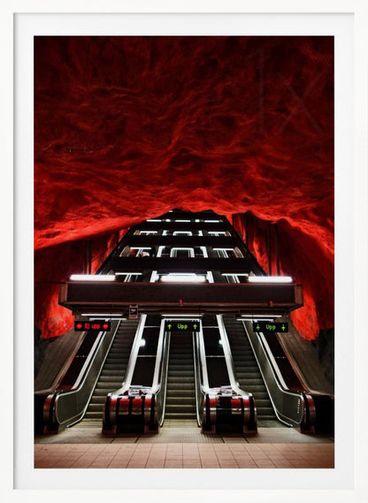 A dramatic low-angle shot looking up a series of escalators in a subway station with a cavernous, rough-textured ceiling glowing an intense, fiery red. Decor
