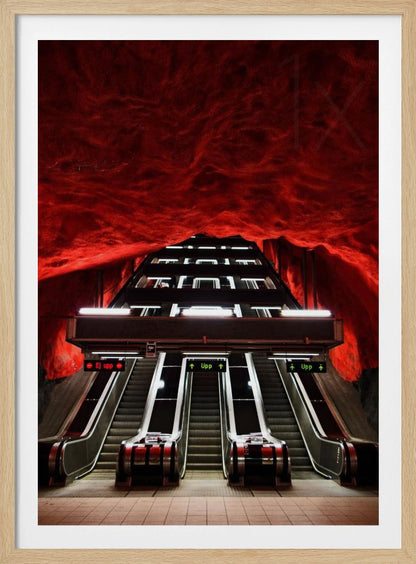 A dramatic low-angle shot looking up a series of escalators in a subway station with a cavernous, rough-textured ceiling glowing an intense, fiery red. Decor
