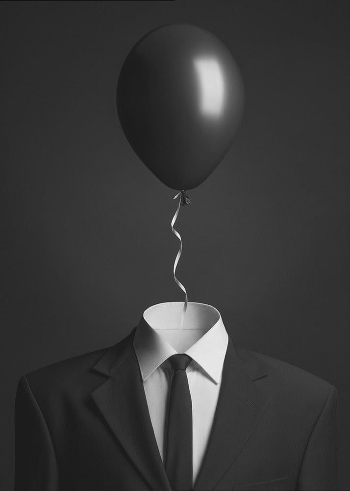 A surreal black and white photograph of a man's suit and tie with a single black balloon floating where the head should be. The curly ribbon from the balloon descends into the white shirt collar. Decor