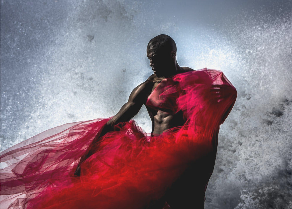 A dramatic photograph of a muscular Black man, mostly in shadow, holding a voluminous, sheer red fabric against a backdrop of splashing white water. The image is encased in a silver frame. Poster