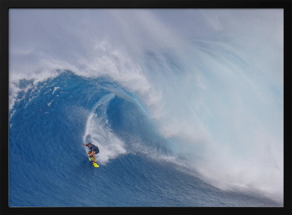 A framed photograph of a professional surfer skillfully riding down the steep face of a massive, cresting blue ocean wave, surrounded by white sea spray. Decor