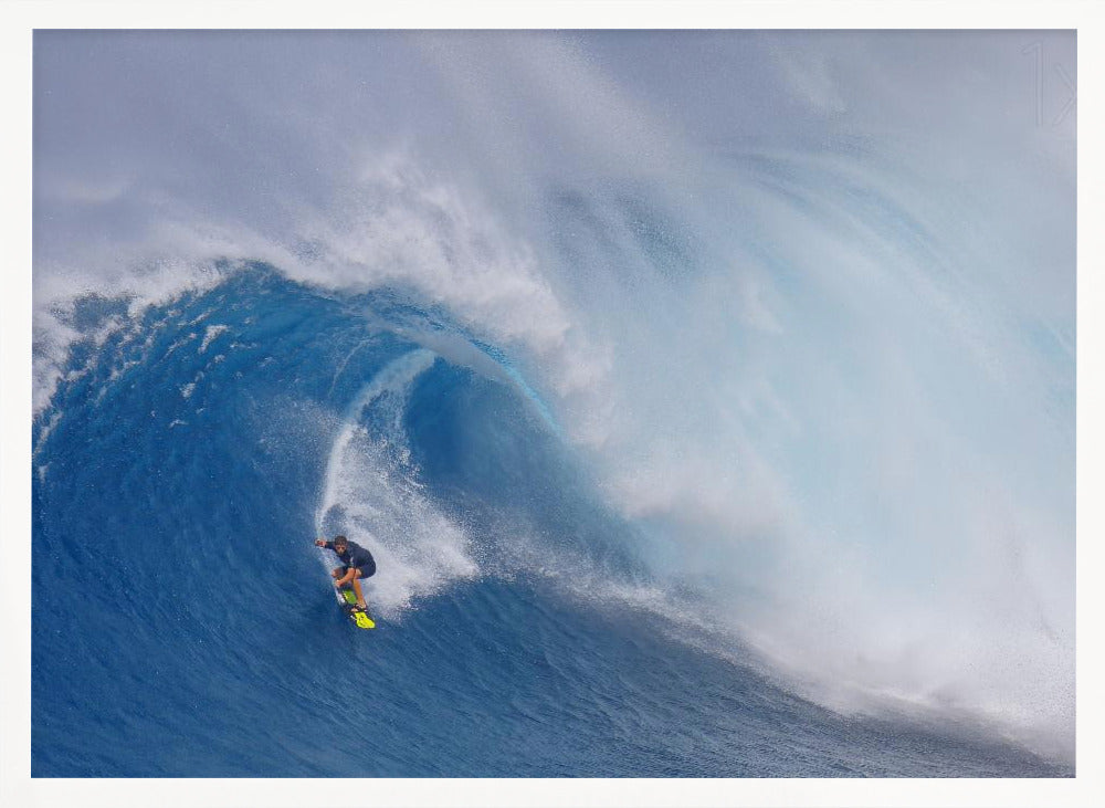 A framed photograph of a professional surfer skillfully riding down the steep face of a massive, cresting blue ocean wave, surrounded by white sea spray. Decor