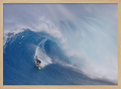 A framed photograph of a professional surfer skillfully riding down the steep face of a massive, cresting blue ocean wave, surrounded by white sea spray. Decor