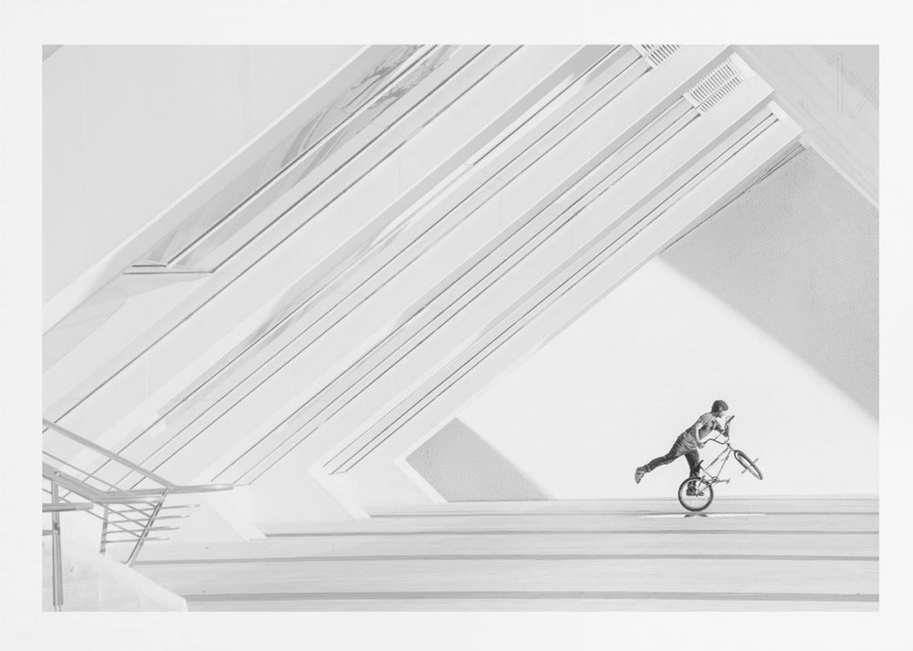 A minimalist black and white photograph in a silver frame, featuring a lone BMX rider performing a trick on the back wheel inside a stark, modern building with strong diagonal architectural lines. Poster