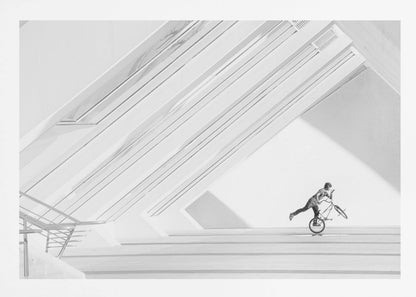 A minimalist black and white photograph in a silver frame, featuring a lone BMX rider performing a trick on the back wheel inside a stark, modern building with strong diagonal architectural lines. Poster