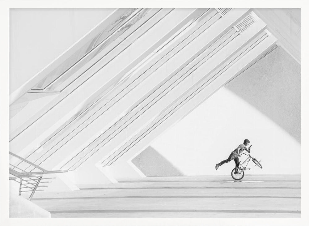 A minimalist black and white photograph in a silver frame, featuring a lone BMX rider performing a trick on the back wheel inside a stark, modern building with strong diagonal architectural lines. Poster