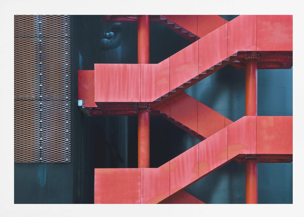 A framed abstract architectural photograph of a bright red industrial staircase zig-zagging against a dark teal wall. The composition highlights the geometric shapes and bold color contrast between the red stairs and the cool-toned background, with a silver mesh panel visible on the left side. Print