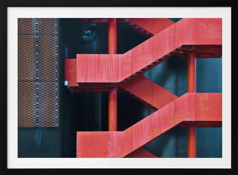 A framed abstract architectural photograph of a bright red industrial staircase zig-zagging against a dark teal wall. The composition highlights the geometric shapes and bold color contrast between the red stairs and the cool-toned background, with a silver mesh panel visible on the left side. Print