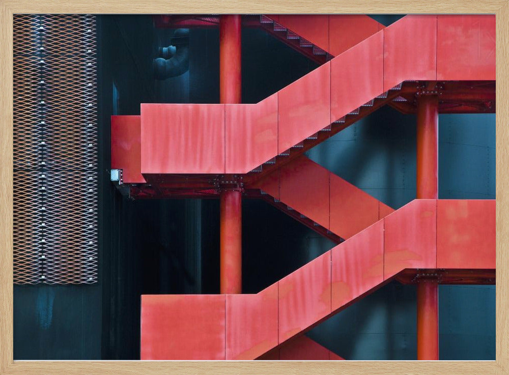 A framed abstract architectural photograph of a bright red industrial staircase zig-zagging against a dark teal wall. The composition highlights the geometric shapes and bold color contrast between the red stairs and the cool-toned background, with a silver mesh panel visible on the left side. Print