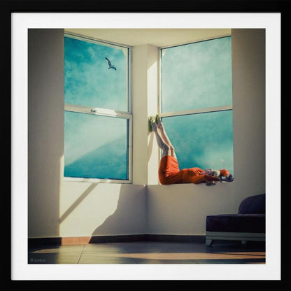 A surreal photograph of a woman in a bright orange dress lying on a wide, sunlit windowsill with her legs up against the wall. Through the large windows, a single bird is seen flying in a vibrant teal sky. The image, presented in a light wood frame, captures a moment of quiet contemplation and escape. Wall Art
