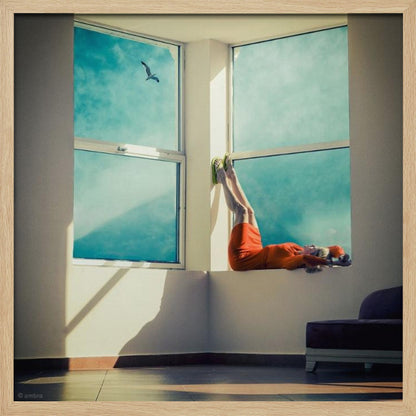 A surreal photograph of a woman in a bright orange dress lying on a wide, sunlit windowsill with her legs up against the wall. Through the large windows, a single bird is seen flying in a vibrant teal sky. The image, presented in a light wood frame, captures a moment of quiet contemplation and escape. Wall Art