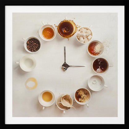 A creative flat lay photograph of a clock made from coffee cups and ingredients. Twelve white cups are arranged in a circle on a white background, each representing an hour and filled with different coffee-related items like beans, honey, sugar cubes, and various stages of coffee with milk splashing. In the center, two silver spoons form the hands of the clock. The entire image is presented within a light wood frame. Decor
