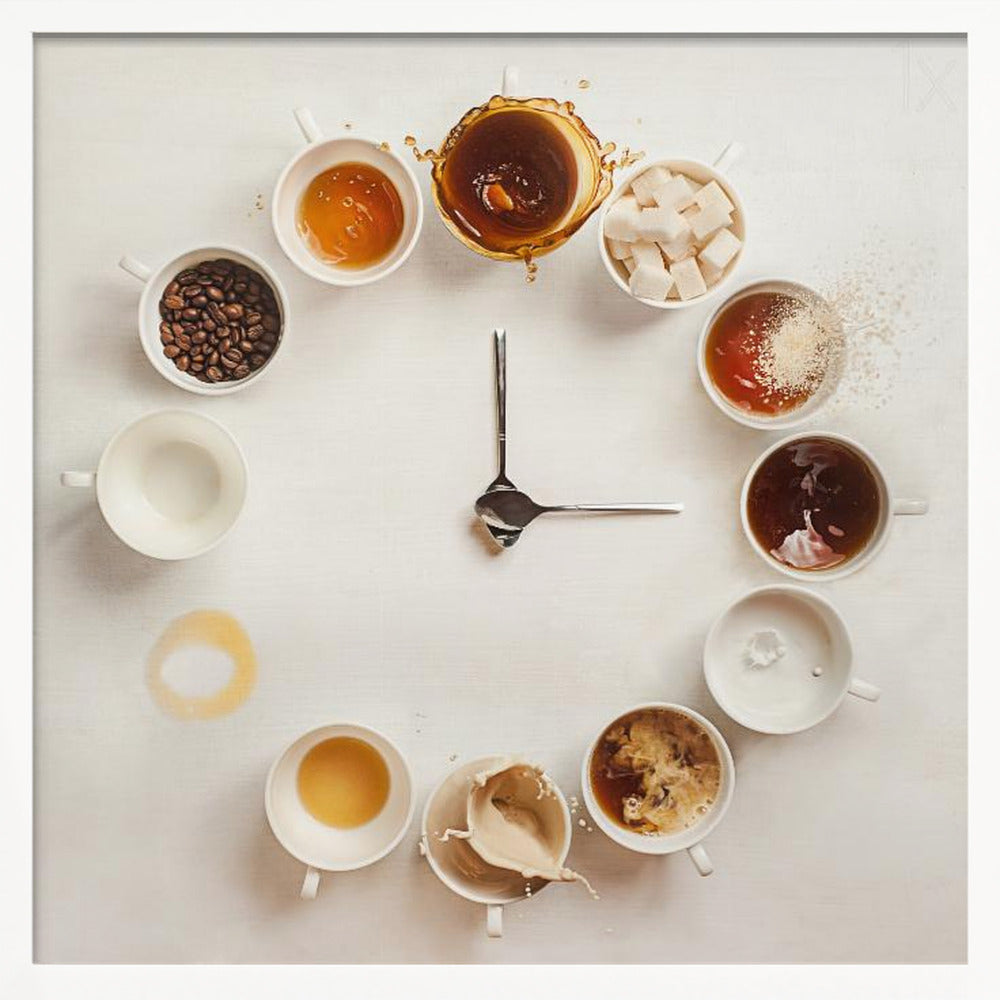 A creative flat lay photograph of a clock made from coffee cups and ingredients. Twelve white cups are arranged in a circle on a white background, each representing an hour and filled with different coffee-related items like beans, honey, sugar cubes, and various stages of coffee with milk splashing. In the center, two silver spoons form the hands of the clock. The entire image is presented within a light wood frame. Decor