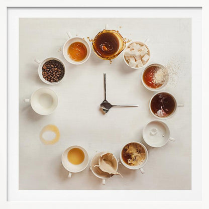 A creative flat lay photograph of a clock made from coffee cups and ingredients. Twelve white cups are arranged in a circle on a white background, each representing an hour and filled with different coffee-related items like beans, honey, sugar cubes, and various stages of coffee with milk splashing. In the center, two silver spoons form the hands of the clock. The entire image is presented within a light wood frame. Decor