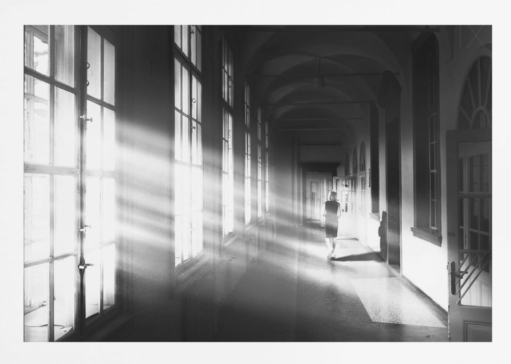 A black and white photograph of a woman walking away down a long, dark hallway. Bright shafts of sunlight pour through large windows on the left, creating a dramatic interplay of light and shadow on the floor and walls. Poster