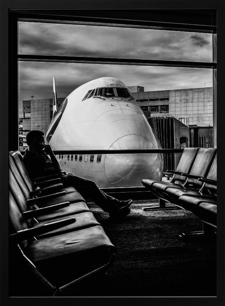 A dramatic black and white photograph of a silhouetted person sitting in an airport departure lounge, waiting for their flight. Through the large window, the enormous nose of a Boeing 747 jumbo jet is visible up close, dominating the view under a cloudy sky. Artwork