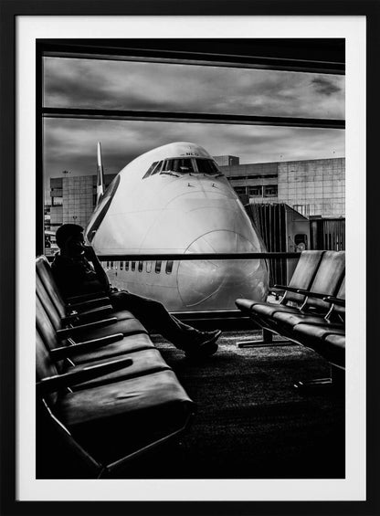 A dramatic black and white photograph of a silhouetted person sitting in an airport departure lounge, waiting for their flight. Through the large window, the enormous nose of a Boeing 747 jumbo jet is visible up close, dominating the view under a cloudy sky. Artwork