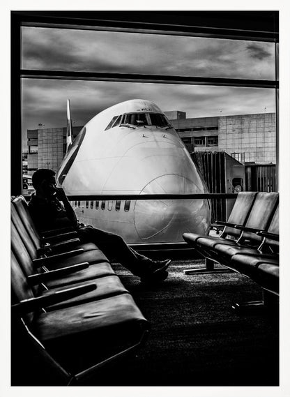 A dramatic black and white photograph of a silhouetted person sitting in an airport departure lounge, waiting for their flight. Through the large window, the enormous nose of a Boeing 747 jumbo jet is visible up close, dominating the view under a cloudy sky. Artwork