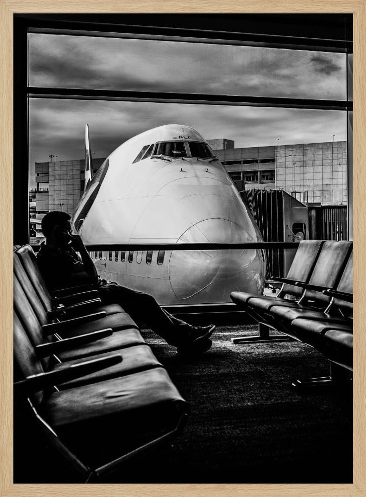A dramatic black and white photograph of a silhouetted person sitting in an airport departure lounge, waiting for their flight. Through the large window, the enormous nose of a Boeing 747 jumbo jet is visible up close, dominating the view under a cloudy sky. Artwork