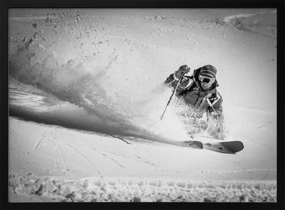 A framed, black and white action shot of a skier making a sharp turn on a snowy slope, sending a large spray of powder into the air. The skier is leaning into the turn, fully kitted out in winter gear including goggles and a beanie. Artwork