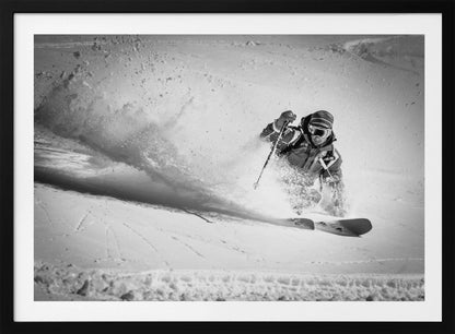 A framed, black and white action shot of a skier making a sharp turn on a snowy slope, sending a large spray of powder into the air. The skier is leaning into the turn, fully kitted out in winter gear including goggles and a beanie. Artwork