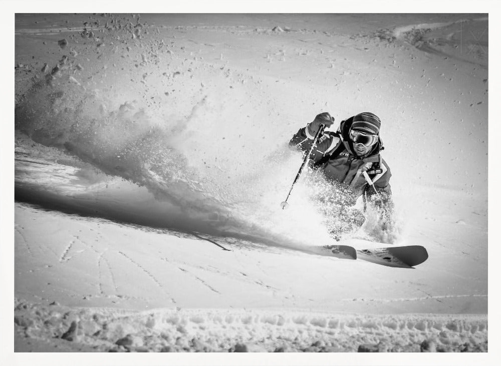 A framed, black and white action shot of a skier making a sharp turn on a snowy slope, sending a large spray of powder into the air. The skier is leaning into the turn, fully kitted out in winter gear including goggles and a beanie. Artwork