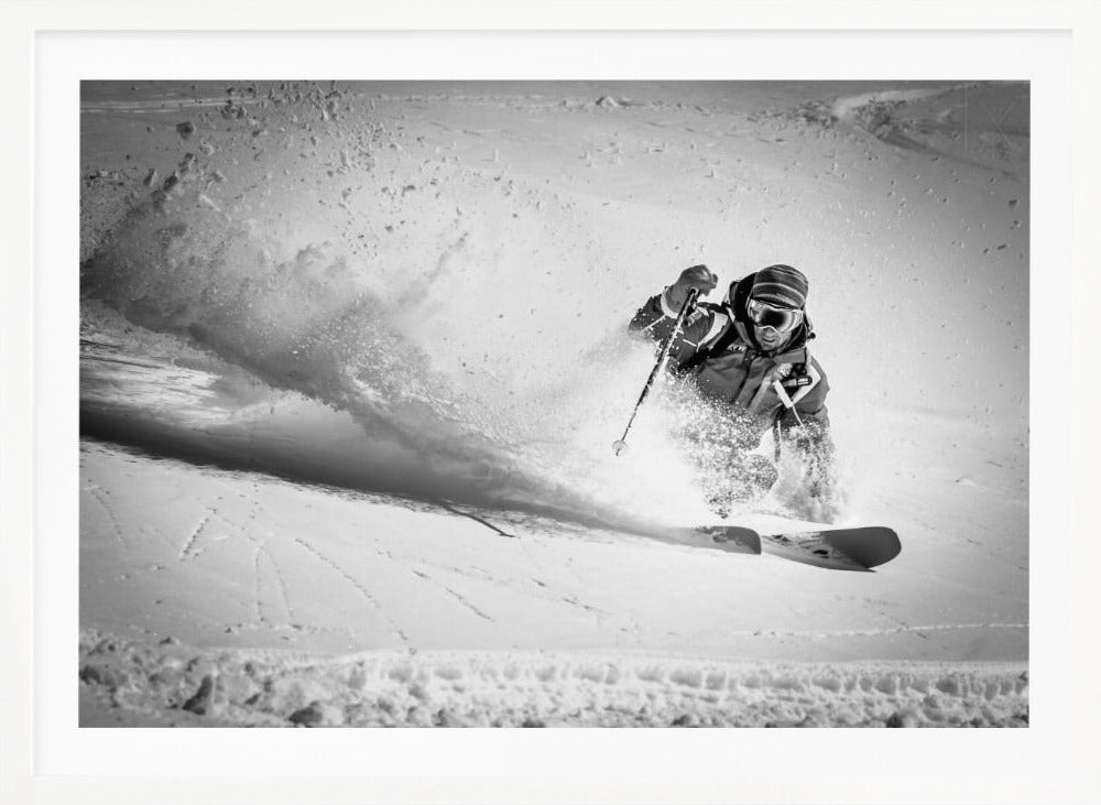 A framed, black and white action shot of a skier making a sharp turn on a snowy slope, sending a large spray of powder into the air. The skier is leaning into the turn, fully kitted out in winter gear including goggles and a beanie. Artwork