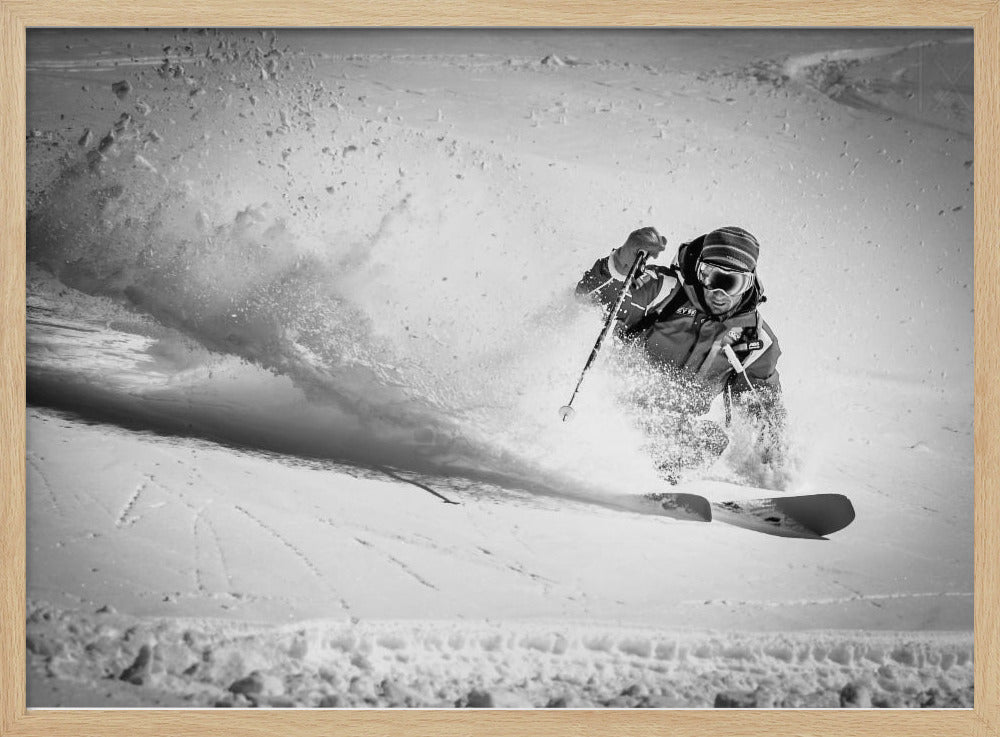 A framed, black and white action shot of a skier making a sharp turn on a snowy slope, sending a large spray of powder into the air. The skier is leaning into the turn, fully kitted out in winter gear including goggles and a beanie. Artwork