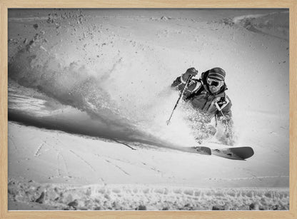 A framed, black and white action shot of a skier making a sharp turn on a snowy slope, sending a large spray of powder into the air. The skier is leaning into the turn, fully kitted out in winter gear including goggles and a beanie. Artwork