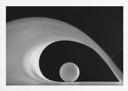 A dramatic black and white still life photo featuring a golf ball set against a stark black background. A large, abstract white shape swirls gracefully over the ball, creating a dynamic, wave-like composition. The image is presented within a silver frame. Decor