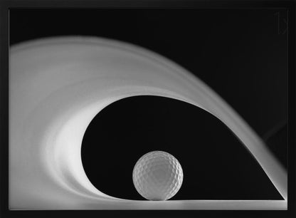 A dramatic black and white still life photo featuring a golf ball set against a stark black background. A large, abstract white shape swirls gracefully over the ball, creating a dynamic, wave-like composition. The image is presented within a silver frame. Decor