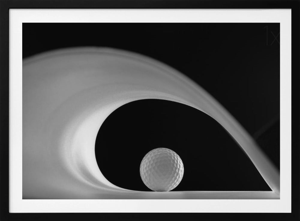 A dramatic black and white still life photo featuring a golf ball set against a stark black background. A large, abstract white shape swirls gracefully over the ball, creating a dynamic, wave-like composition. The image is presented within a silver frame. Decor