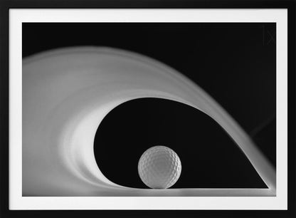 A dramatic black and white still life photo featuring a golf ball set against a stark black background. A large, abstract white shape swirls gracefully over the ball, creating a dynamic, wave-like composition. The image is presented within a silver frame. Decor