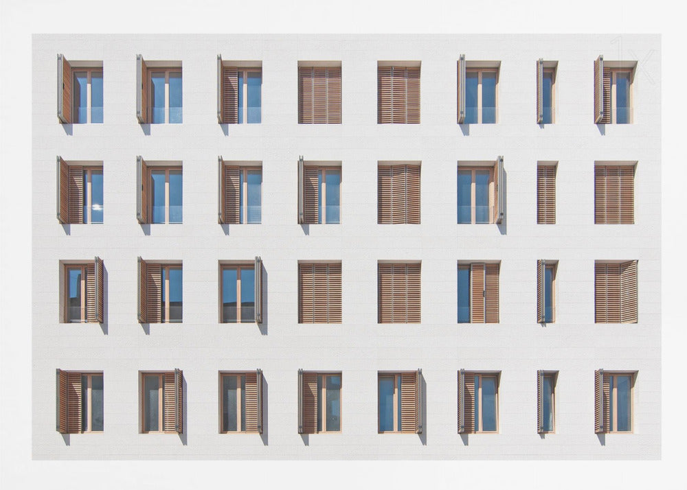 A symmetrical architectural photo of a modern white building facade featuring a grid of twenty-eight windows with wooden louvered shutters, some open and some closed, creating a varied pattern, all within a brushed silver frame. Decor