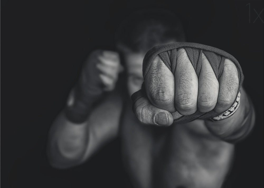 A dramatic black and white close-up photograph of a boxer's wrapped fist punching towards the camera. The fighter's body and other fist are blurred in the background, creating a powerful and intense mood. Print
