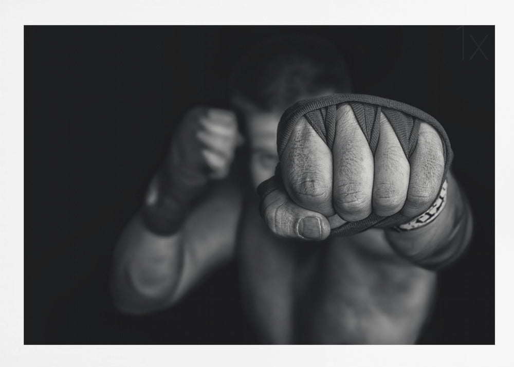 A dramatic black and white close-up photograph of a boxer's wrapped fist punching towards the camera. The fighter's body and other fist are blurred in the background, creating a powerful and intense mood. Print
