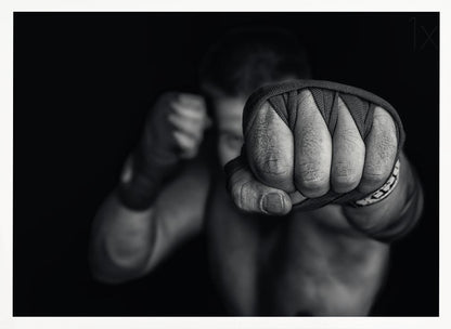 A dramatic black and white close-up photograph of a boxer's wrapped fist punching towards the camera. The fighter's body and other fist are blurred in the background, creating a powerful and intense mood. Print