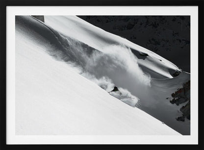 A dramatic black and white photograph of a skier speeding down a steep, snow-covered mountain, kicking up a large cloud of powder. The image is framed with a brushed silver border. Decor