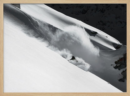 A dramatic black and white photograph of a skier speeding down a steep, snow-covered mountain, kicking up a large cloud of powder. The image is framed with a brushed silver border. Decor