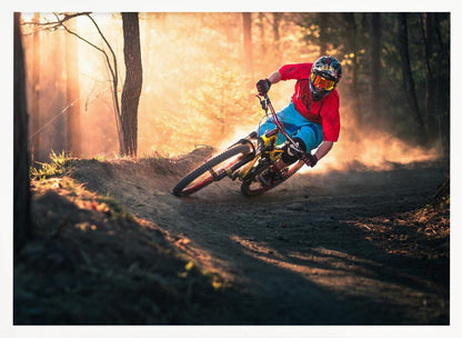 A mountain biker in a red shirt, blue shorts, and full-face helmet leans sharply into a dusty turn on a dirt trail in a forest. The setting sun casts a warm, golden light through the trees, creating a dramatic, backlit effect. Wall Art
