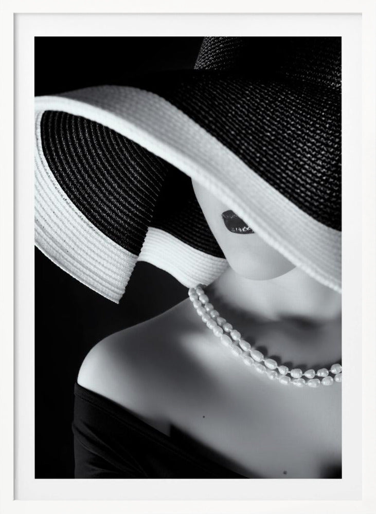 A glamorous black and white close-up photo of a woman wearing a large, striped sun hat that hides her eyes, revealing only her dark lips. She wears a pearl necklace and an off-the-shoulder top against a dark background, creating a mysterious and elegant mood. Wall Art