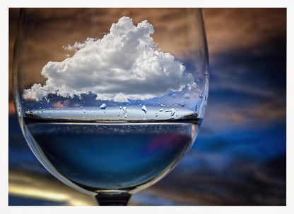 A surreal close-up of a wine glass holding blue liquid and a single white cloud, with water droplets on the glass, set against a blurred background and enclosed in a silver frame. Print