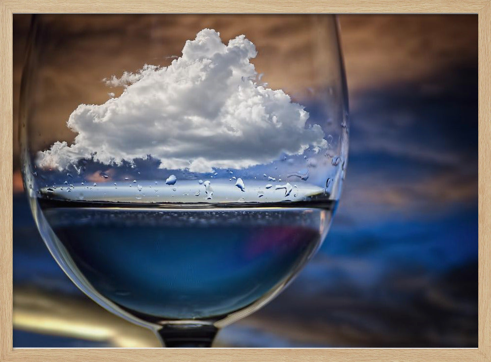 A surreal close-up of a wine glass holding blue liquid and a single white cloud, with water droplets on the glass, set against a blurred background and enclosed in a silver frame. Print