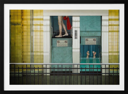 A surreal, framed artwork depicting two teal-colored vertical cabins against a yellow tiled wall. In the left cabin, a person's bare legs are visible as they hold a red towel. In the right cabin, which is filled with water, only a pair of feet can be seen submerged. A black railing is in the foreground, adding to the strange, layered composition. Artwork