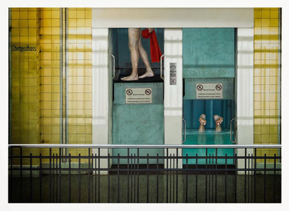 A surreal, framed artwork depicting two teal-colored vertical cabins against a yellow tiled wall. In the left cabin, a person's bare legs are visible as they hold a red towel. In the right cabin, which is filled with water, only a pair of feet can be seen submerged. A black railing is in the foreground, adding to the strange, layered composition. Artwork