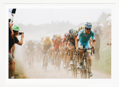 A framed photograph of a peloton of professional cyclists racing down a dusty dirt road. The lead cyclist is in sharp focus, wearing a bright turquoise uniform and a helmet, with other racers in yellow and red jerseys blurred behind him. A spectator on the left is taking a photo with a smartphone. Poster