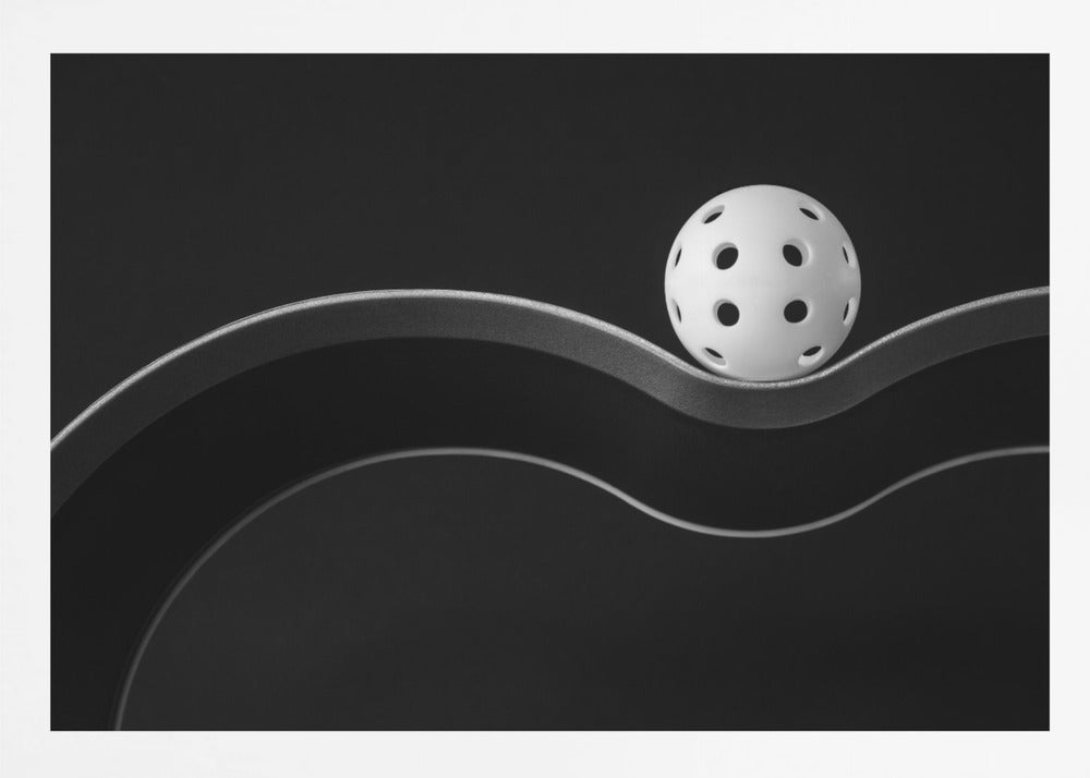 A minimalist black and white photograph of a white pickleball resting perfectly balanced on a thick, wavy, textured line against a solid black background. Below it, a thin white line mimics the curve. The entire piece is framed in silver. Poster