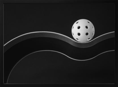 A minimalist black and white photograph of a white pickleball resting perfectly balanced on a thick, wavy, textured line against a solid black background. Below it, a thin white line mimics the curve. The entire piece is framed in silver. Poster