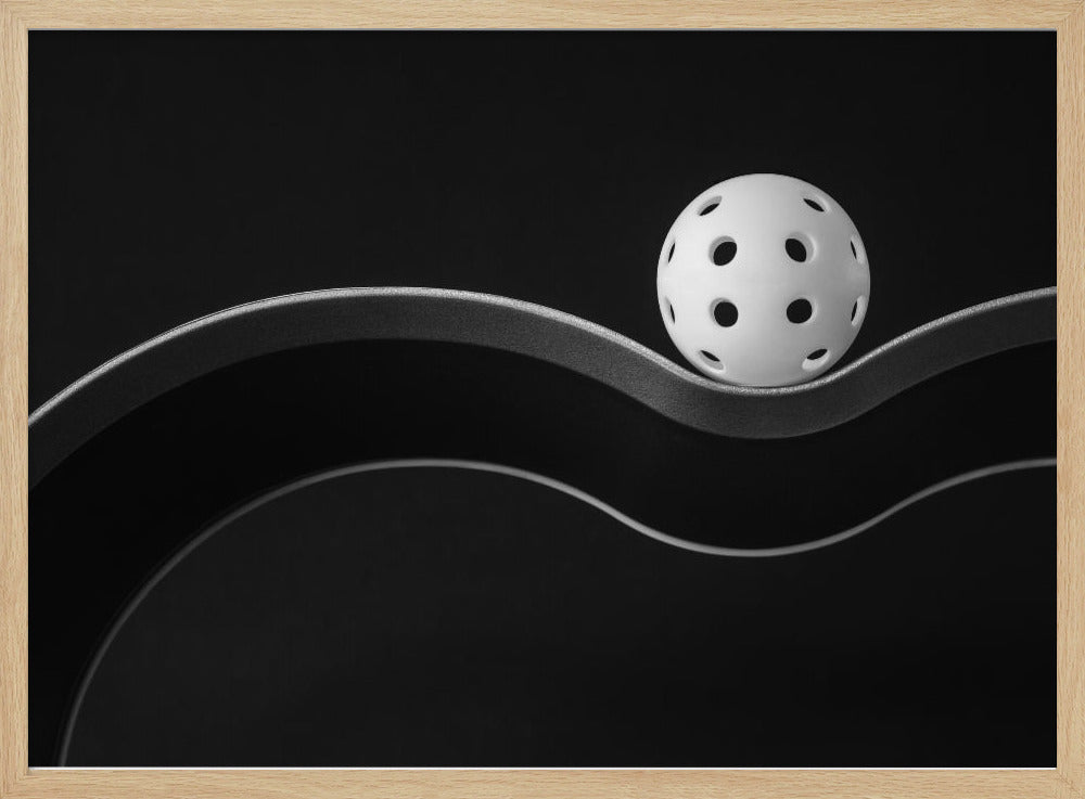 A minimalist black and white photograph of a white pickleball resting perfectly balanced on a thick, wavy, textured line against a solid black background. Below it, a thin white line mimics the curve. The entire piece is framed in silver. Poster
